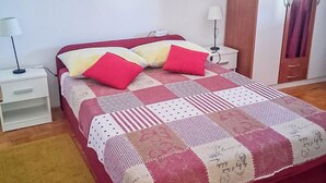 Ein Schlafzimmer mit einem roten Bett, weißen Nachttischen, einem Holzschrank und einer karierten Tagesdecke.