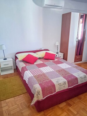 Ein Schlafzimmer mit einem roten Bett, weißen Nachttischen, einem Holzschrank und einer karierten Tagesdecke.