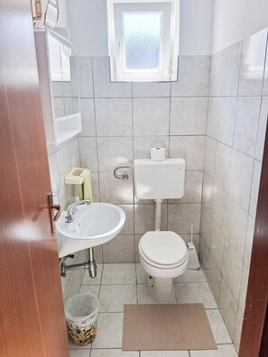Ein kleines Badezimmer mit Toilette, Waschbecken und einem Fenster über der Toilette.