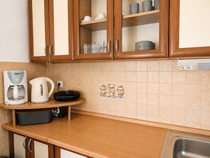 A kitchen with wooden cabinets, a coffee maker, a kettle, and a tiled backsplash. - Apartment Luna (Rogoznica)