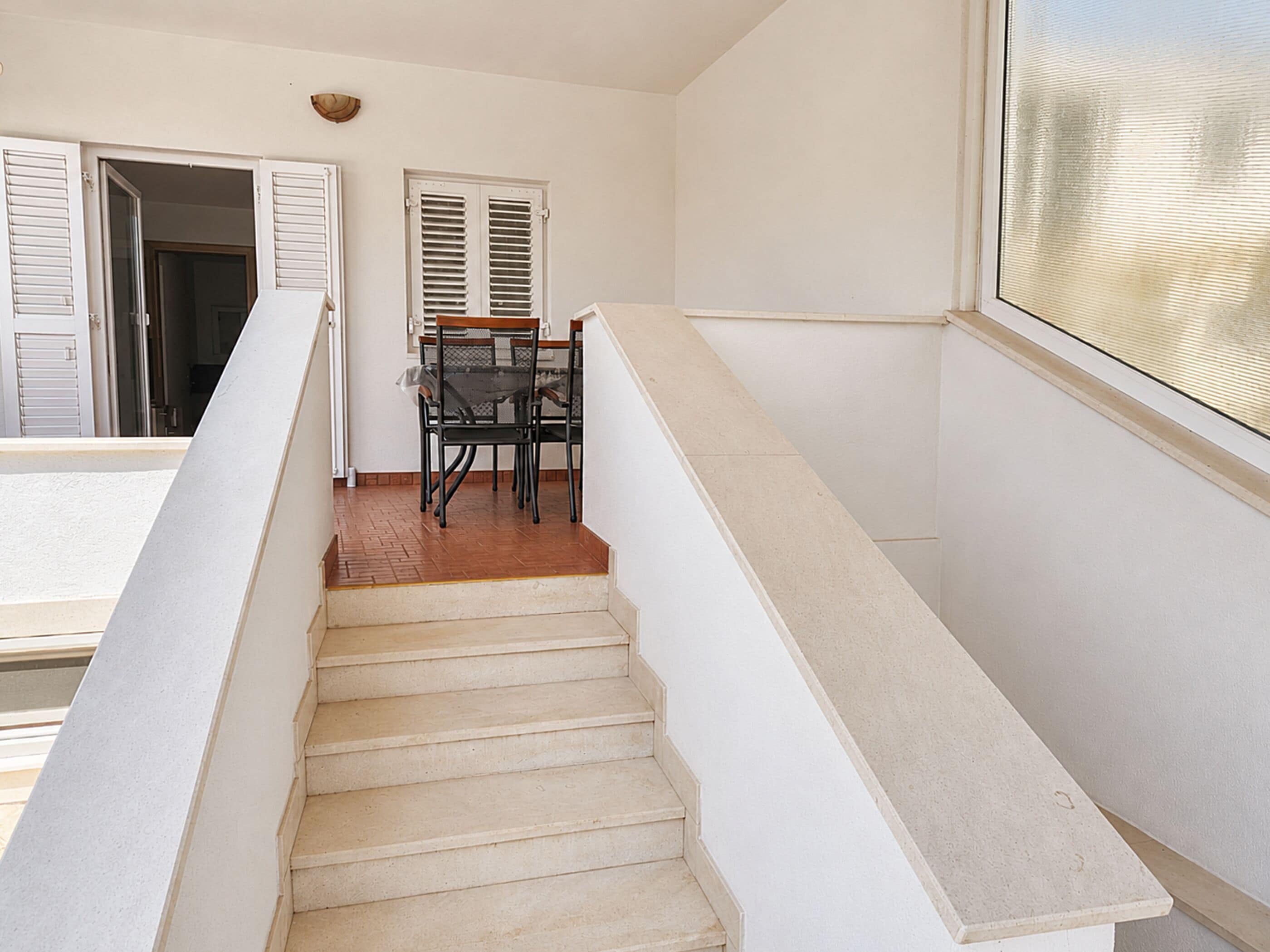 A staircase with a handrail, a dining table with chairs, and a window with blinds.
