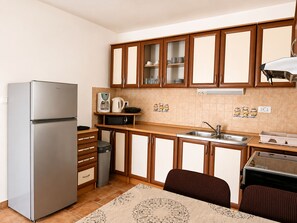 A compact kitchen with a refrigerator, microwave, sink, and wooden cabinets. - Apartment Luna (Rogoznica)