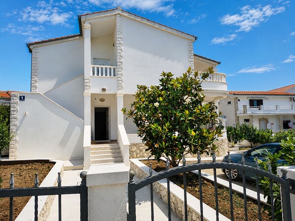 A two-story building with a balcony, a staircase leading to the entrance, and a tree in the foreground. - Apartment Luna (Rogoznica)