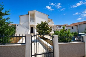 A white building with a balcony, surrounded by a fence and greenery. - Apartment Luna (Rogoznica)