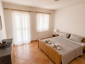 A bedroom with a wooden bed, a nightstand, a lamp, and a window with curtains. - Apartment Luna (Rogoznica)