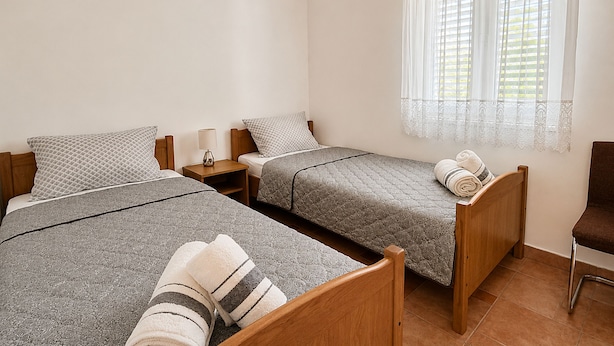 Ein Zimmer mit zwei Betten, einem Nachttisch, einem Sessel und einem Fenster mit Vorhängen.