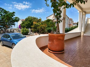A blue car parked near a white building with a curved white wall, a potted plant, and a staircase leading to an upper level. - Apartment Luna (Rogoznica)
