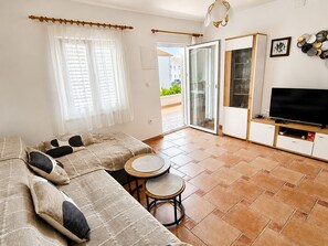 A modern living room with a sofa set, a TV, a small table, and a sliding glass door leading to an outdoor area. - Apartment Luna (Rogoznica)