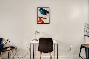 Ein moderner Arbeitsraum mit Schreibtisch, Stuhl und einem gerahmten abstrakten Kunstwerk an der Wand.