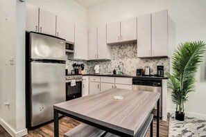 Una cocina moderna con armarios blancos, un refrigerador de acero inoxidable, horno empotrado y cafetera.