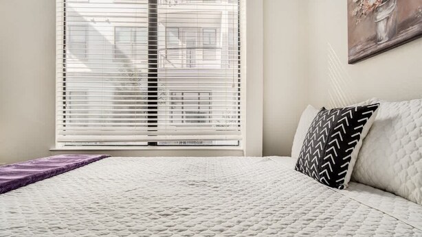 Een slaapkamer met een bed, een raam met zonwering, en een schilderij aan de muur.