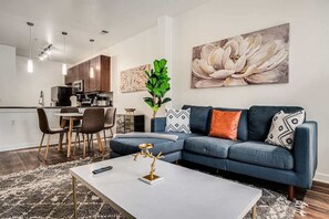 Ein modernes Wohnzimmer mit einem blauen Sofa, einem Couchtisch und einem Essbereich mit Stühlen und einem Tisch.