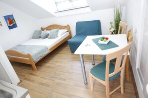 Ett litet rum med en säng, en blå soffa, ett matbord med en stol och ett litet fönster.