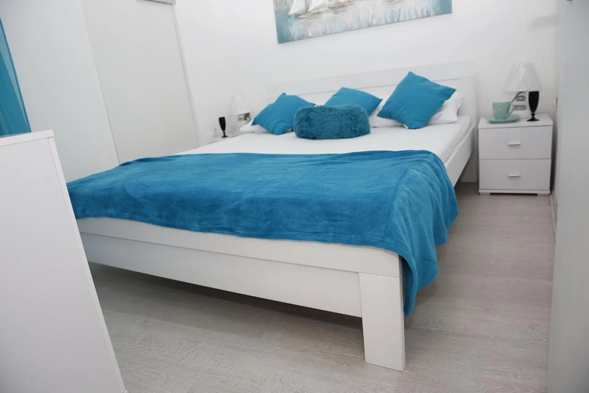 A bedroom with a white bed, blue bedding, and a nightstand with a lamp.