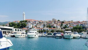A marina with boats docked, a white building with a tower, and a hillside of colorful houses. - Apartment Ines (Novi Vinodolski)