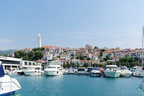 A marina with boats docked, a white building with a tower, and a hillside of colorful houses. - Apartment Ines (Novi Vinodolski)