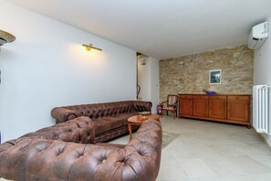 Een woonkamer met een bruine leren bank, een houten salontafel en een stenen muur.