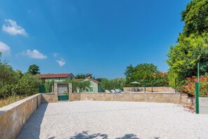 A gravel driveway leading to a gated entrance with a stone wall, a small building with a red roof, and a green fence. - House Barba Frane (Vizinada)