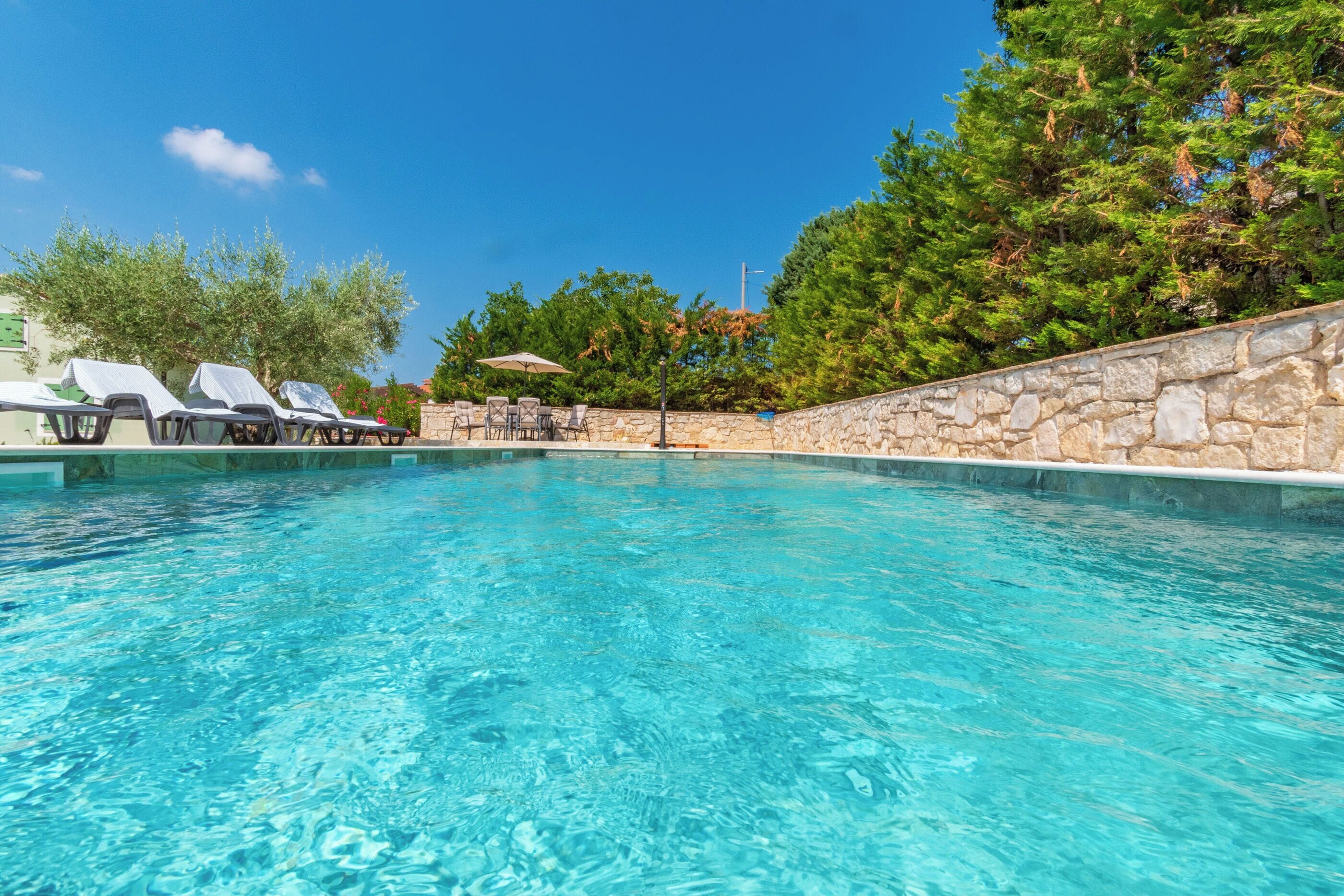 Una piscina nítida amb gandules i una paret de pedra.