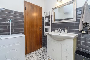 Une salle de bain avec un lavabo blanc, un miroir, un porte-serviettes et une porte.