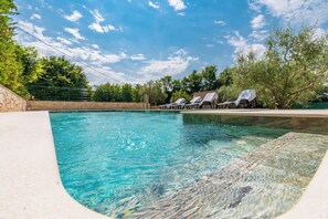 Ein klares Schwimmbecken mit Liegestühlen und einer Steinmauer.