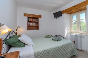 Een slaapkamer met een bed, een nachtkastje met lamp, een boekenkast, een raam met uitzicht en een aan de muur bevestigde televisie.
