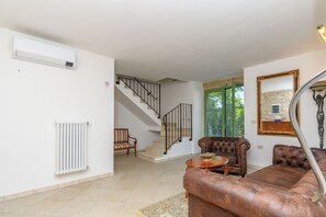 A living room with a brown leather sofa, a wooden coffee table, a radiator, a staircase, and a mirror on the wall. - House Barba Frane (Vizinada)