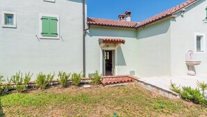 Um edifício com fachada verde clara, telhado em telhas e pequena entrada.