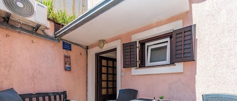 Un patio con mesa, sillas, banco y unidad de aire acondicionado.