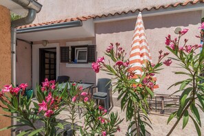 A patio with a table and chairs, a striped umbrella, and pink flowers. - Apartment Leona's Paradise (Opatija)