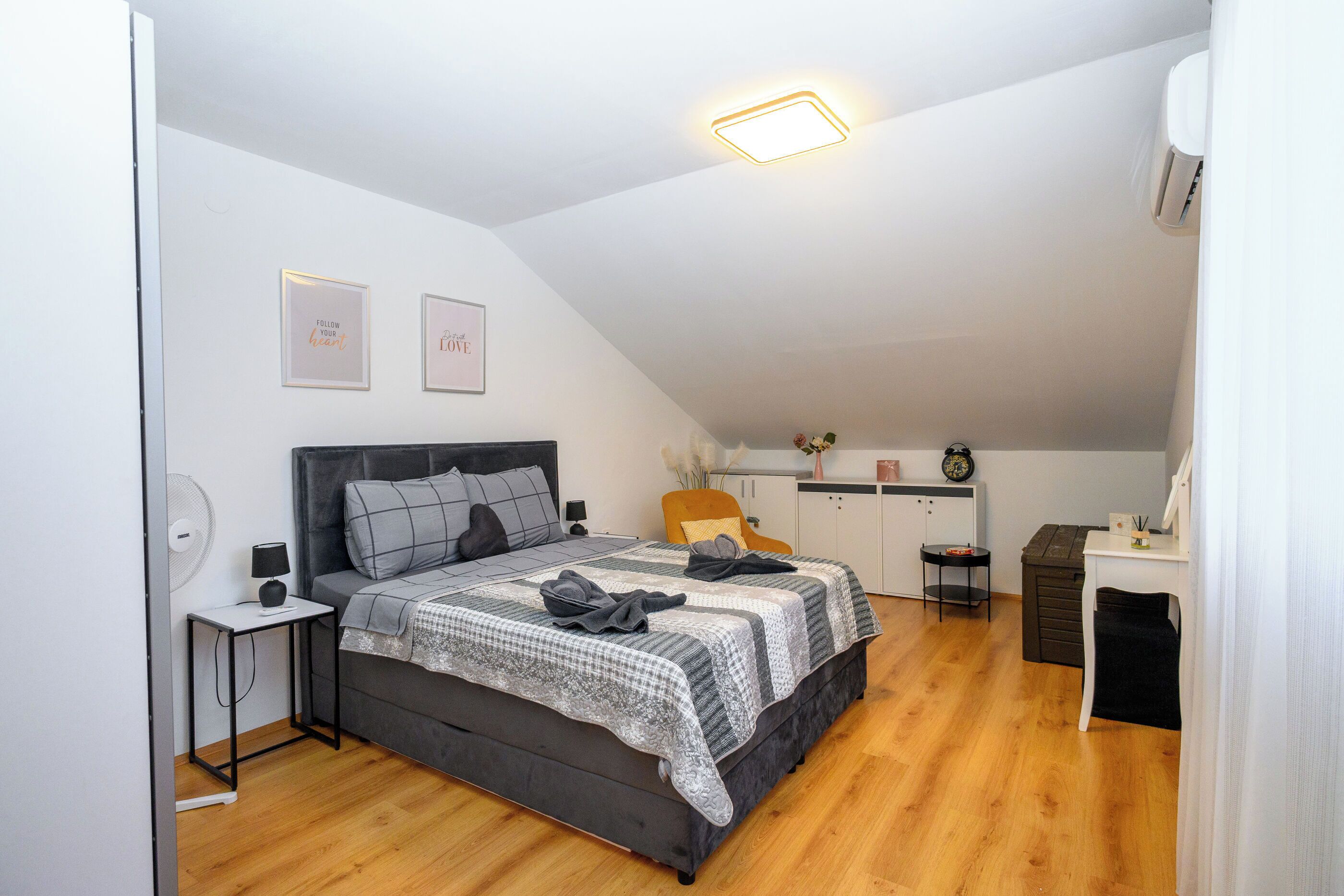Une chambre à coucher comprenant un lit, des tables de chevet, un ventilateur fixé au mur et un luminaire au plafond.