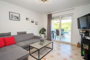 A modern living room with a grey sofa, a coffee table, a TV, and a balcony with outdoor furniture. - Apartment Blue Oasis (Novi Vinodolski)