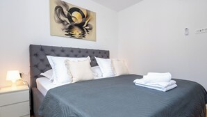 Un lit bien fait, avec une tête de lit grise, des oreillers blancs et une couvre-lit grise.