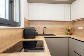 A modern kitchen with a built-in stove, a sink, and a wooden backsplash. - Apartment Seaview Terrace (Podstrana)