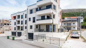 Un immeuble résidentiel à plusieurs étages, doté de balcons, d’un garage et d’une voiture garée devant.