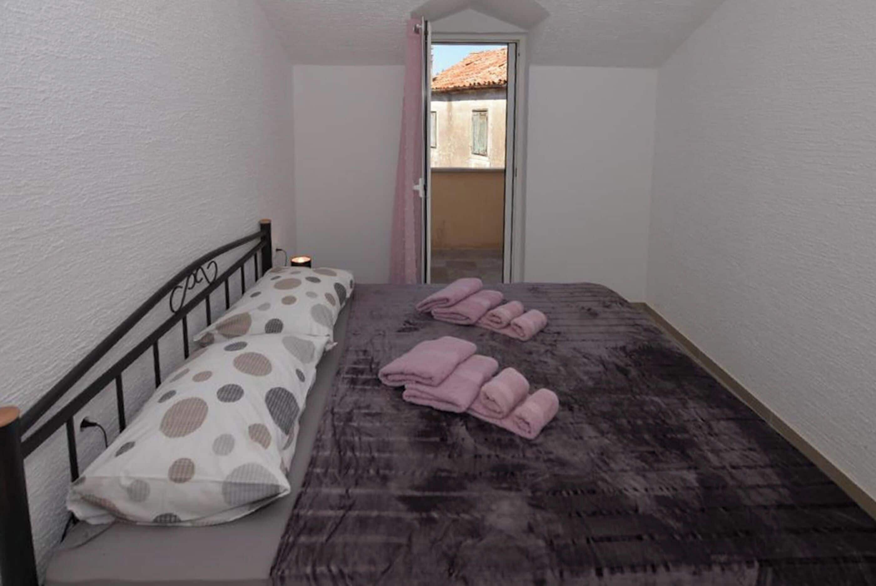 Un dormitorio pequeño con una cama, un almohadón y una toalla enrollada.