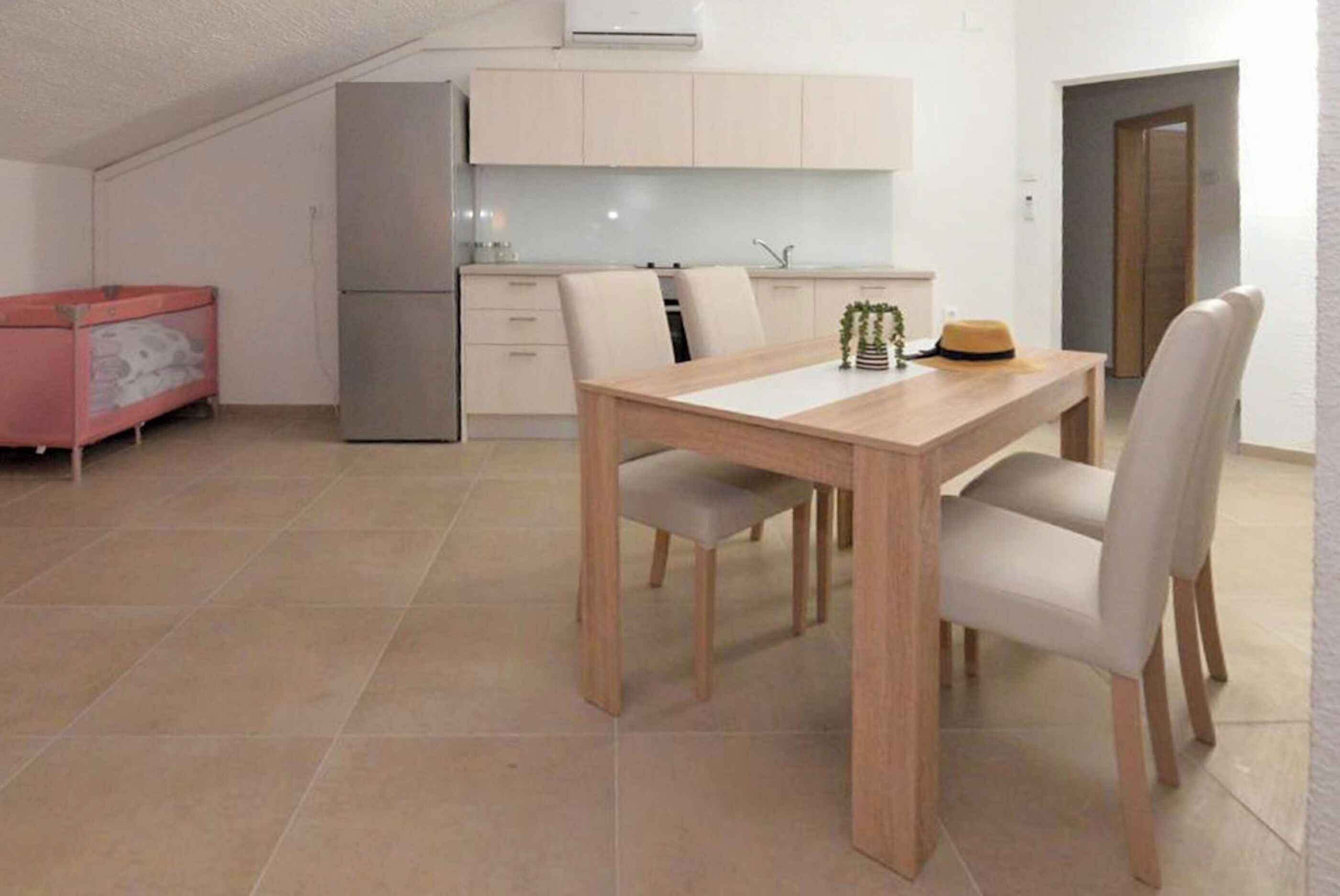 A modern kitchen with white cabinets, a dining table with chairs, and a small refrigerator.