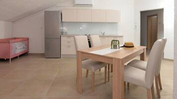 A modern kitchen with white cabinets, a dining table with chairs, and a small refrigerator.
