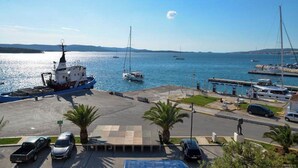 A marina with boats, a dock, and a parking area with cars and palm trees. - Apartment Nikola Centar (Biograd na Moru)