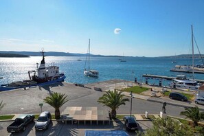 A marina with boats, a dock, and a parking area with cars and palm trees. - Apartment Nikola Centar (Biograd na Moru)