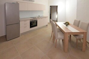 A compact kitchen with a refrigerator, oven, and sink, a dining table with chairs, and a hallway leading to another room. - Apartment Nikola Centar (Biograd na Moru)