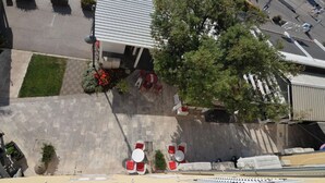 An aerial view of a building with a flat roof, outdoor seating area with red chairs and tables, and a large tree in front. - Apartment Nikola Centar (Biograd na Moru)