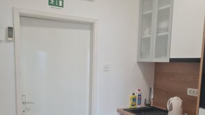 Una pequeña cocina americana con una puerta blanca, un equipo de aire acondicionado arriba y un lavamanos con productos de limpieza.