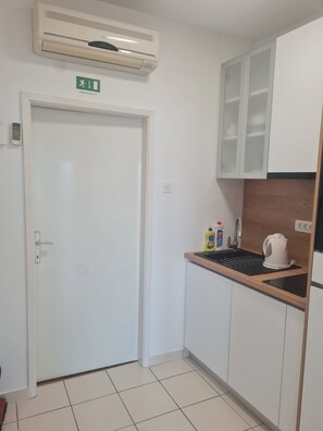 A small kitchenette with a white door, an air conditioning unit above, and a sink with cleaning supplies. - Apartments Damir (Omis)