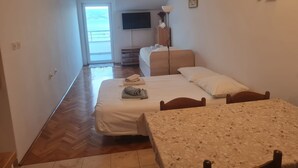 Habitación de hotel con dos camas, una mesa, un televisor y vista al mar a través de un amplio ventanal.