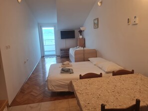 A hotel room with two beds, a table, a TV, and a view of the sea through a large window. - Apartments Damir (Omis)