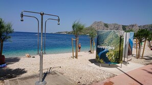 A beach with a clear blue sea, a rocky mountain in the background, and a large sign with '#loveomis'. - Apartments Damir (Omis)