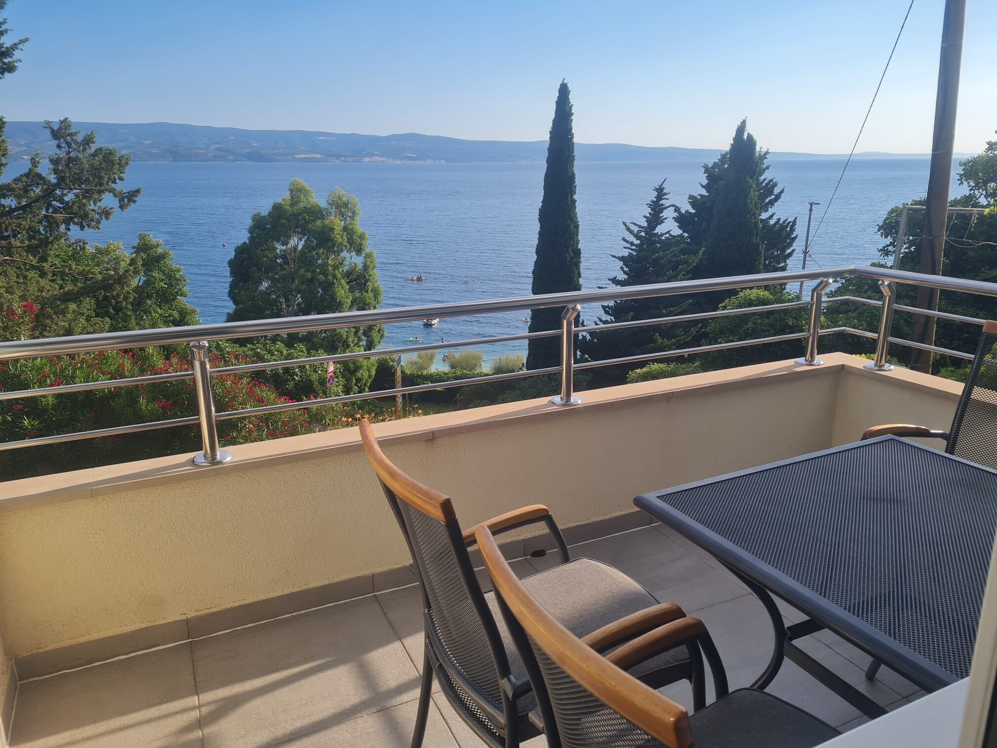 Ein Balkon mit Tisch und Stühlen, mit Blick auf ein Gewässer und sanfte Hügel in der Ferne.