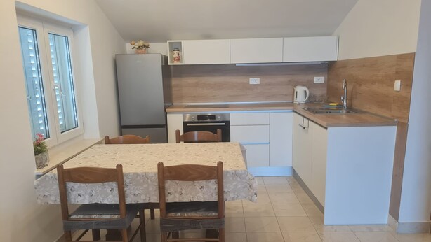 Una cocina compacta con mesa, sillas, refrigerador, lavavajillas y pileta.