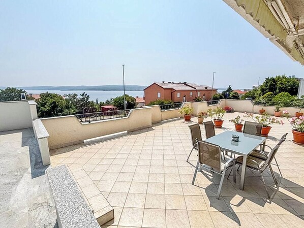 Una terrassa al terrat amb una taula i cadires, plantes en testos i vista al mar.